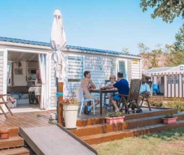 Terrasse en bois avec table et personnes déjeunant au camping Les Jardins de la Mer