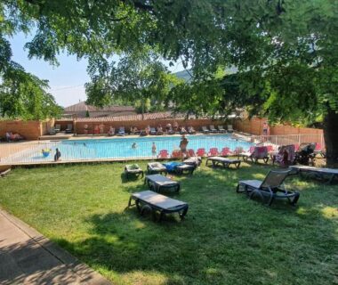 Pelouse et piscine entourée d'arbres au Camping Les Lavandes