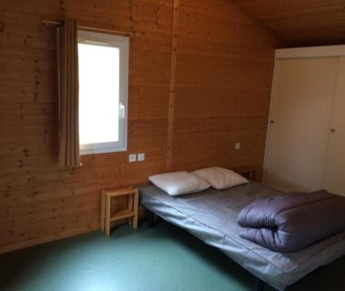 Intérieur de chambre en bois avec lit et armoire au Camping Les Lupins