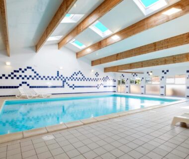 Piscine couverte intérieure avec puits de lumière et transats au Camping Les Mizottes