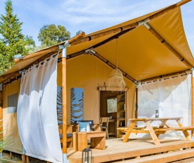 Terrasse en bois avec table pique-nique et rideaux du lodge au Camping Les Mizottes