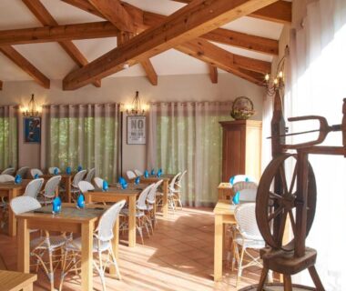Salle à manger avec tables en bois et poutres apparentes au Camping Les Oliviers