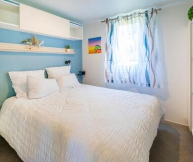 Chambre double lumineuse avec lit et rideaux au Camping Les Oyats