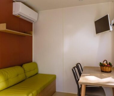 Intérieur locatif avec canapé vert et coin repas dans le Camping Les Pins - Bord de mer