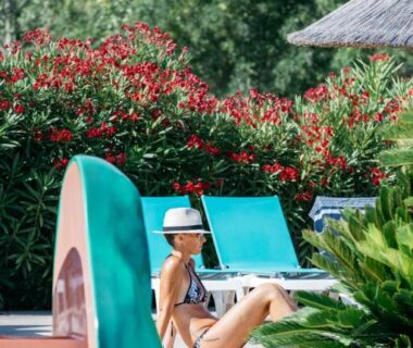 Bord de la piscine avec transats et parasol en paille au Camping Les Pins – Bord de mer