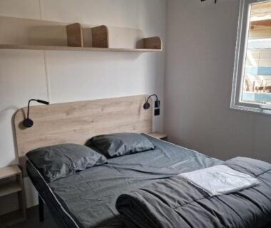 Chambre avec lit double et lampes murales dans le camping Les P'tites Maisons dans la Prairie