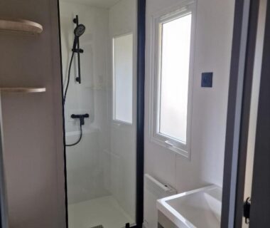 Salle d'eau avec douche vitrée et fenêtre au Camping Les P'tites Maisons dans la Prairie