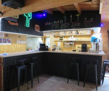 Bar intérieur avec comptoir et tabourets au Camping Les P'tites Maisons dans la Prairie