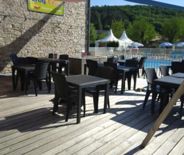 Terrasse en bois avec tables et vue sur piscine au Camping Les Rives du Céou
