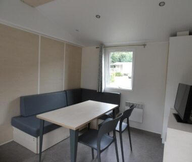 Coin repas intérieur avec banquette table et télévision dans le mobil-home du Camping Les Sables Blancs