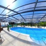 Piscine couverte avec transats et petite structure de jeux en bois au camping Les Terrasses de Dordogne