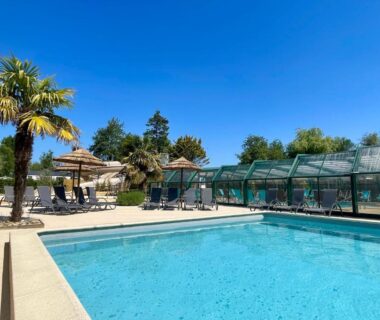 Piscine extérieure bordée de palmiers et transats au camping Les Tourterelles