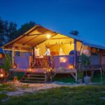 Tente sur terrasse en bois éclairée au crépuscule au Camping Les Vertes Feuilles
