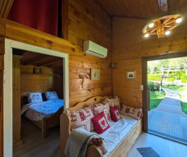 Intérieur de chalet en bois avec canapé et chambre visible au Camping L'imprévu