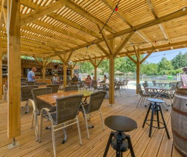 Terrasse couverte avec tables et piscine au Camping L'imprévu
