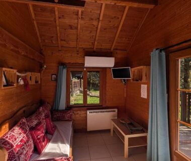 Intérieur de chalet en bois avec coin salon télévision climatisation et fenêtres au Camping L'imprévu