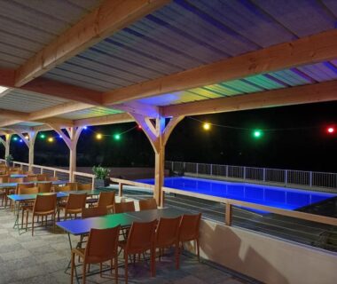 Terrasse couverte avec tables et piscine éclairée du Camping L'oasis Du Berry