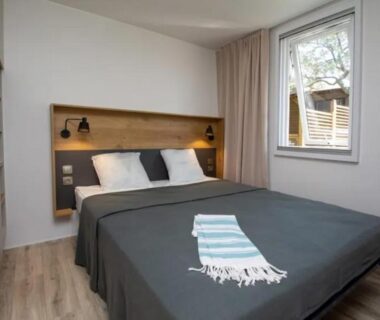 Chambre avec lit double, fenêtre et rangement au Camping Mas De Pierredon