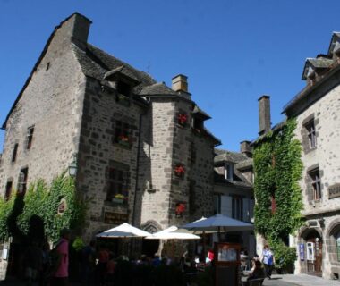 Place villageoise avec terrasses et parasols dans le Cantal au Camping Moulin De Chaules