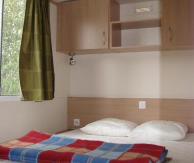 Intérieur de chambre avec lit double et couvertures du Camping Moulin de Collonge