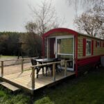 Terrasse en bois et mobil home rouge dans un coin herbeux au Camping Moulin de Collonge