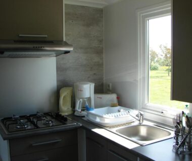 Coin cuisine équipé avec évier et gazinière donnant sur pelouse dans le mobil-home du Camping Moulin de Collonge