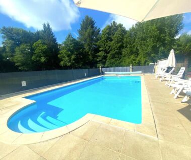 Piscine extérieure avec transats et parasol entourée d'arbres au Camping Moulin du Pommier
