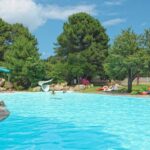Piscine extérieure avec toboggan et transats entourée d'arbres au Camping Mulinacciu