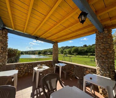 Terrasse couverte avec tables et chaises face à l'étang au Camping Naturiste Tikayan Petit Arlane