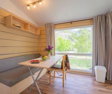Coin repas lumineux avec fenêtre sur la verdure au Camping New Rabioux