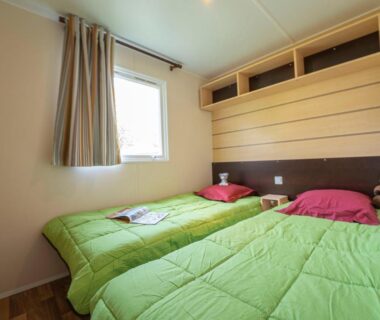 Intérieur de chambre avec deux lits simples et fenêtre dans le mobile home du Camping New Rabioux