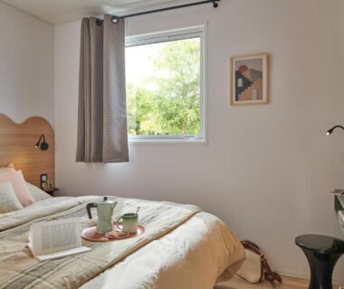 Chambre avec lit et fenêtre donnant sur la verdure au Camping O'Aka