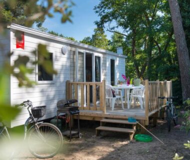 Terrasse de mobil-home avec table et chaises sous les arbres au Camping Officiel Siblu le Montourey