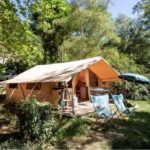 Emplacement ombragé avec tente lodge et chaises pliantes au Camping Onlycamp Le Petit Bocage