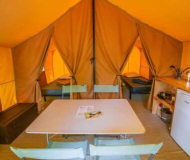 Intérieur de tente avec table chaises lits et coin cuisine au Camping Onlycamp Le Petit Bocage