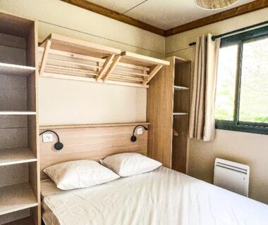 Chambre avec lit double, étagères et fenêtre dans le mobil-home du Camping Onlycamp Le Pont Romain
