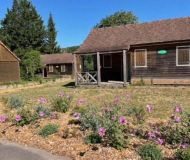 Façade de chalets en bois avec parterres fleuris au Camping Onlycamp Le Pont Romain