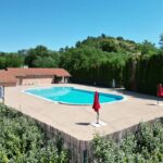 Piscine extérieure avec parasols et terrasse entourée de végétation au Camping Onlycamp Le Pré