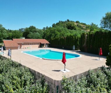 Piscine extérieure avec parasols et terrasse entourée de végétation au Camping Onlycamp Le Pré