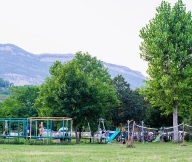 Prairie avec aire de jeux et montagnes en arrière-plan au Camping Onlycamp Les Tuillères