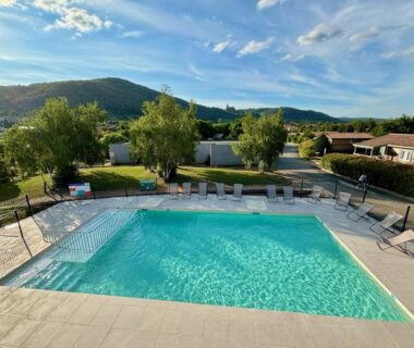 Piscine extérieure avec transats et collines en arrière-plan au Camping Onlycamp Pierre & Sources