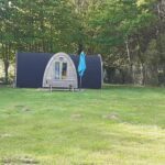 Pelouse avec pod en bois et parasol bleu au Camping Onlycamp Port Sainte Marie