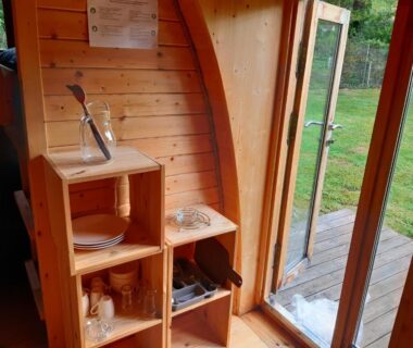 Intérieur kitchenette en bois avec évier et étagères et porte ouverte vers pelouse du Camping Onlycamp Port Sainte Marie