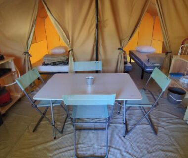 Intérieur de tente avec table chaises lits télévision et réfrigérateur au Camping Onlycamp du Rouergue