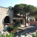 Façade en pierre avec pins et fleurs à l'entrée du camping Paduella