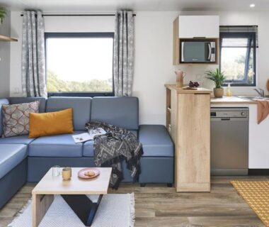 Salon avec canapé d'angle et kitchenette dans le mobil-home du Camping Paradis Le Grand’ R