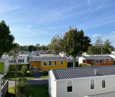Allée de mobil-homes colorés et arbres sous ciel bleu au Camping Paradis Le Royon