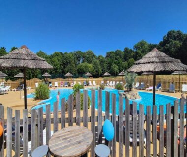 Espace piscine extérieur avec parasols en paille au Camping Paradis du Quinquis