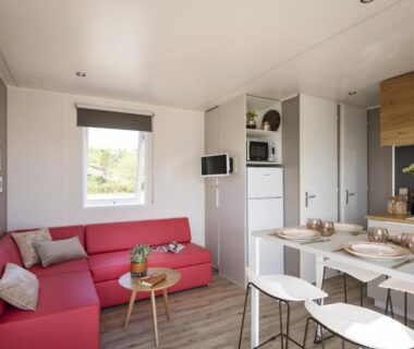 Séjour avec canapé rouge et coin cuisine dans le Camping Paradis du Quinquis