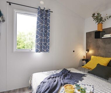 Chambre avec lit double et fenêtre sur la verdure au Camping Paradis le Rocher de la Granelle